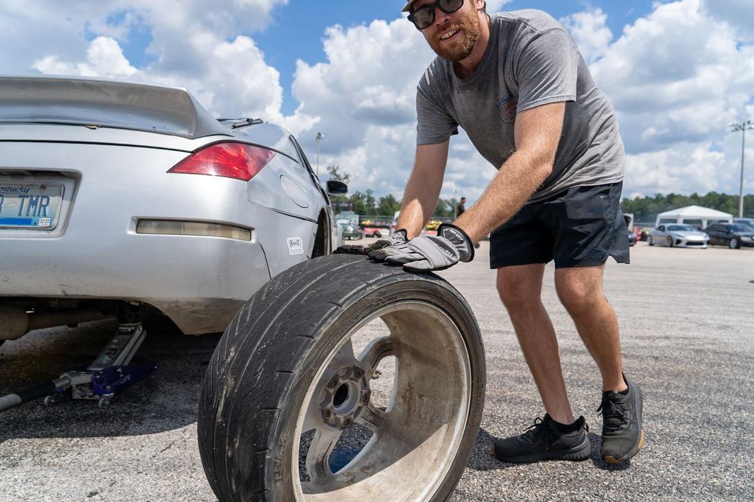 Crew member rolling a worn drift tire in the pits