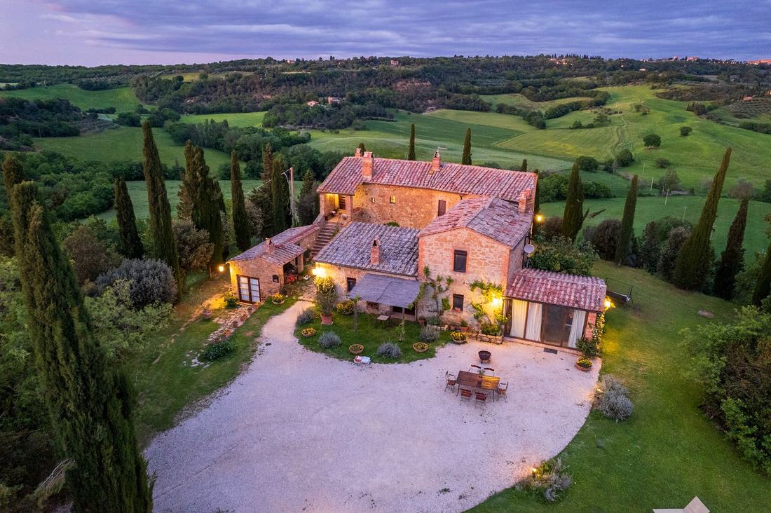 Stone farmhouse among cypress trees at dusk, seen from above