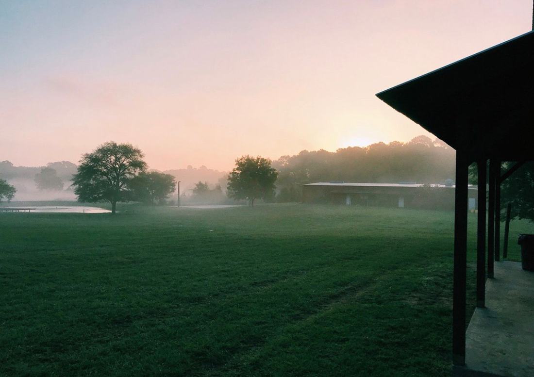 Foggy field at sunrise beside a covered porch