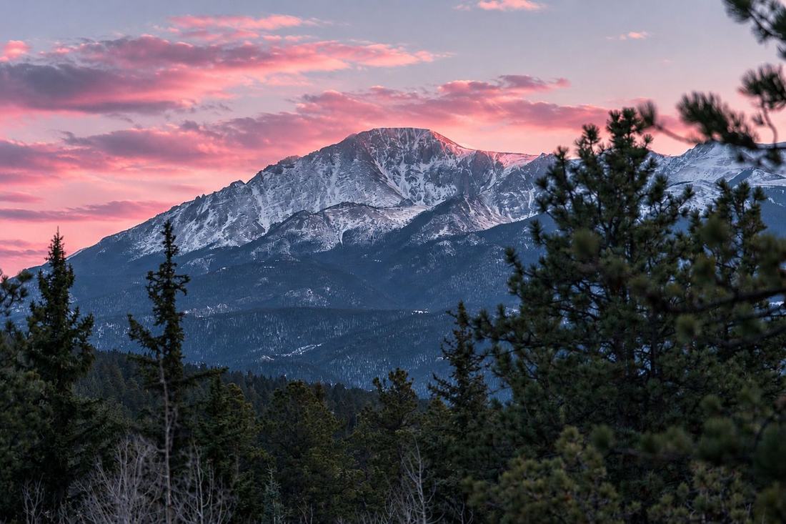 Snowy mountain peak under pink sunset clouds