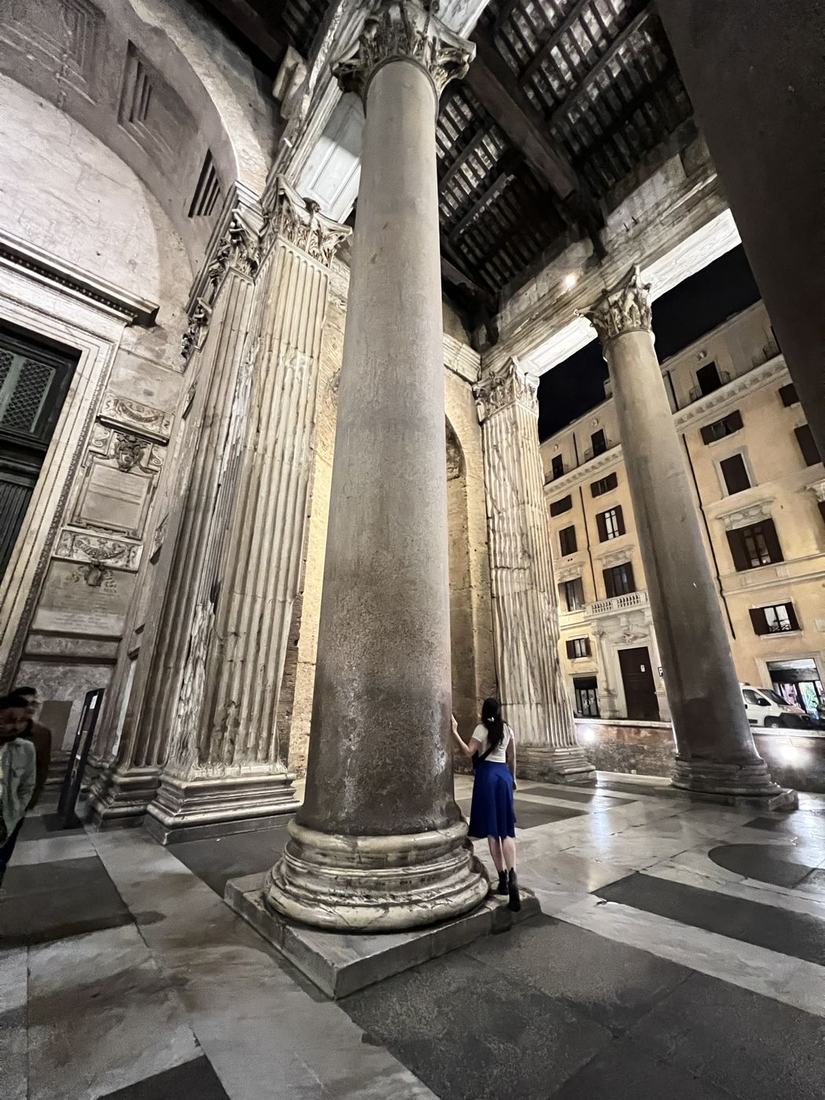 Woman beside a giant column under a lit classical portico at night