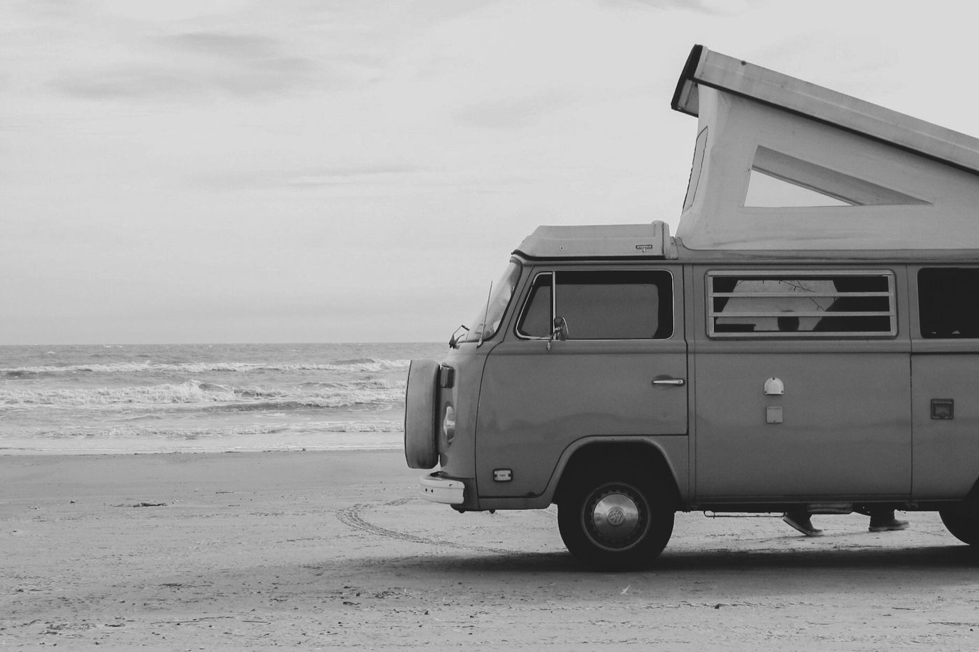 Black and white photo of a pop-top camper van parked on a beach
